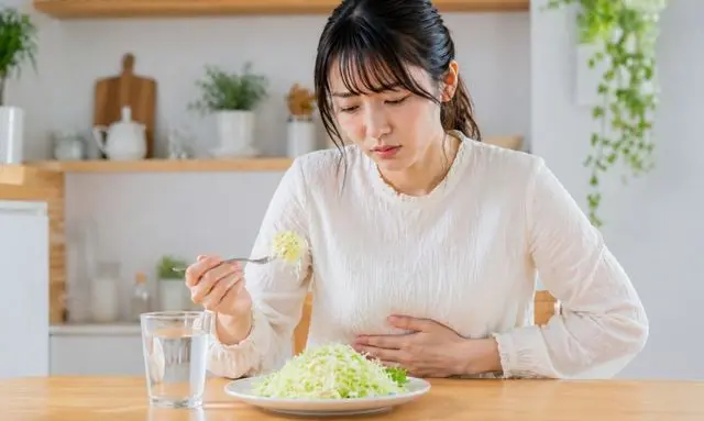 苦いキャベツを食べてお腹の不調を感じる女性の様子