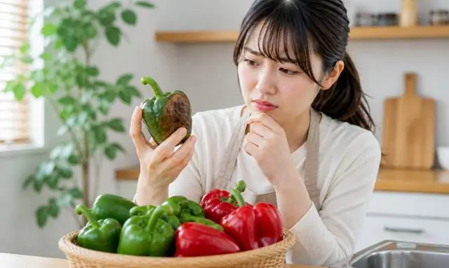 傷んだピーマンをチェックする女性と腐敗のサインのイメージ